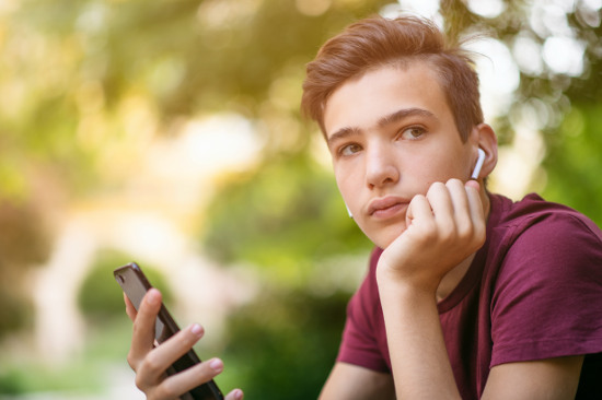 Close-up portrait of a thoughtful unhappy teenage boy with smartphone, outdoors.
